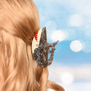 Detail of shark-shaped marble grey hair claw clip on blonde hair with beach background
