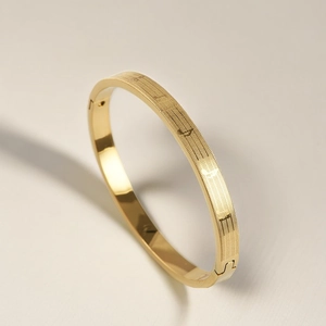 Close-up of golden titanium steel oval bracelet showing engraved musical notes and grid