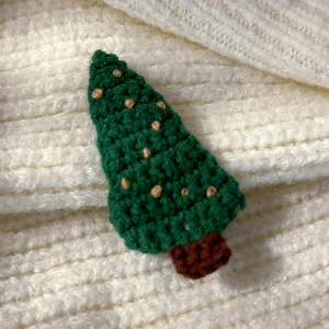 Macro shot of hand-knitted green Christmas tree hair clip with beige pom-poms decor