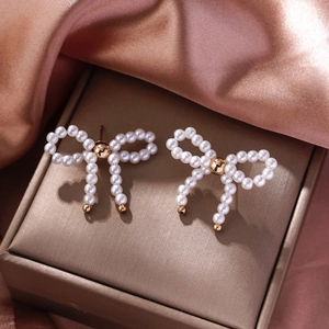 Detail view of pearl bow earrings with gold beads on a champagne jewelry box lid