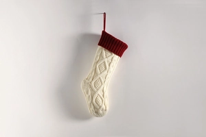 Close-up of cream knitted Christmas stocking with red cuff and textured diamond pattern