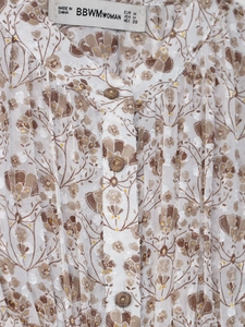 Détail du chemisier en mousseline fleurie avec col montant, volants et boutons en bois brun