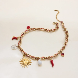 Detail of gold chain necklace with red woven cord and colorful charms on beige surface