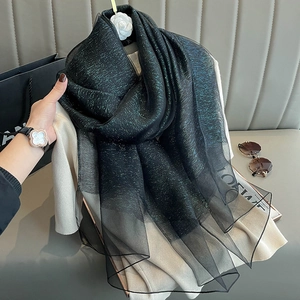 Close-up of black silk scarf with gold thread detail held by hand in a chic setting