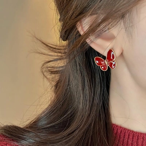 Dettaglio di un orecchino a farfalla rosso scuro con bordo dorato indossato da modella