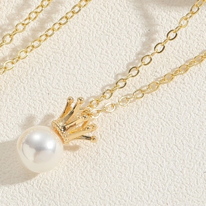 Close-up of a gold crown pendant with a round white pearl on a delicate fine chain necklace