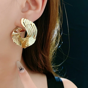 Macro shot of large golden spiral earring with wavy texture worn by a fashion model
