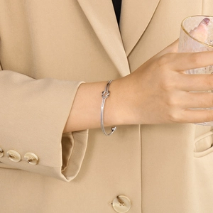Bracelet jonc argenté avec nœud minimaliste porté sur poignet avec veste camel