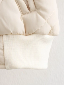 Détail du tissu matelassé en losanges crème avec poignets en maille côtelée de veste