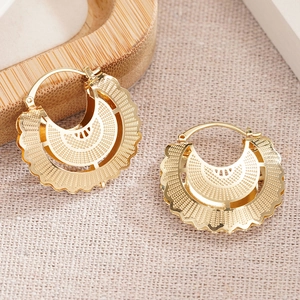Detail of gold hollow floral earrings with ethnic engraving on linen background