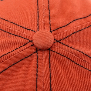 Detailed macro view of orange baseball cap crown with contrast black stitching and eyelets