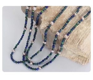 Detail of faceted phoenix lapis and freshwater pearl necklace draped on natural stone