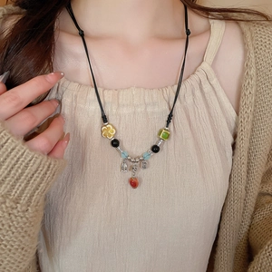 Detail of retro ceramic necklace featuring red apple pendant and silver Nafu charm