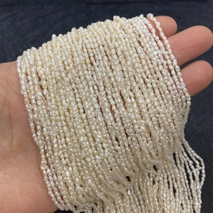 Hand holding multiple strands of small 2-3mm white irregular rice freshwater pearls