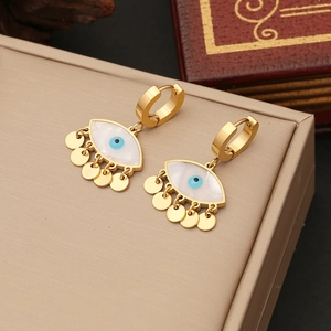 Detail of gold evil eye earrings with dangling charms on a beige jewelry display case