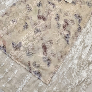 Detailed macro view of beige canvas bag featuring purple butterfly prints and white lace lace