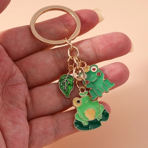 Detail of a gold keychain featuring cartoon green frogs and leaf enamel charms
