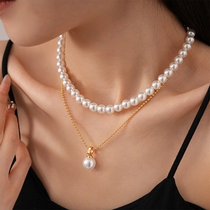 Detail of layered gold beaded chain and white pearl necklace on model's neckline