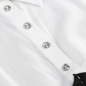 Détail des boutons en strass argentés et bordure satinée noire sur une veste blanche