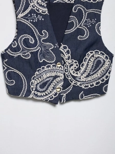 Detail of dark blue denim vest with white paisley embroidery and gold buttons