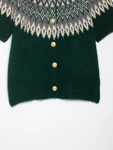 Close-up of green Fair Isle knit cardigan featuring white geometric patterns and gold buttons