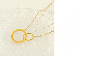 Detail of double-layer gold necklace with interlocking rings and white pearl chain