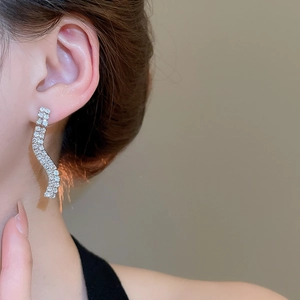Close-up of a silver wavy rhinestone earring worn by a model for a chic luxury look