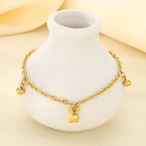 Detail of 18K gold plated anklet with rabbit and bead charms on a white ceramic vase