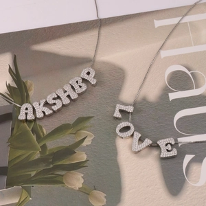 Silver letter pendants AKSHBA and LOVE with zircon inlays on necklaces over a magazine