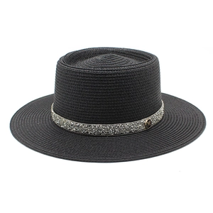 Close-up of black flat top straw hat with silver rhinestone band and golden M logo detail