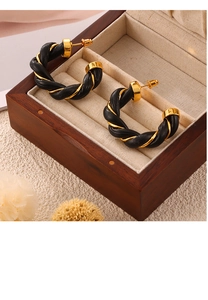 Close-up of C-shaped earrings featuring twisted black leather and gold metal design