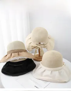 Detail of a wide-brim straw hat featuring an elegant fabric bow on a wooden stand