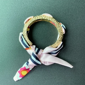 Detail of matte gold bangle with crystal inlay and pink patterned silk scarf knot