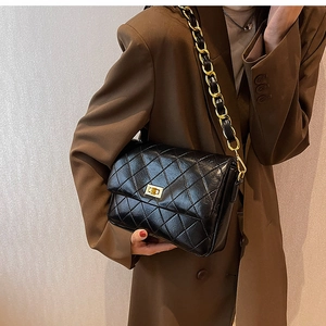 Detail of black quilted shoulder bag with golden chain strap and metallic swivel lock