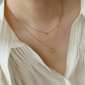 Close-up of double-layer gold necklace with green gemstone and crescent moon pendant