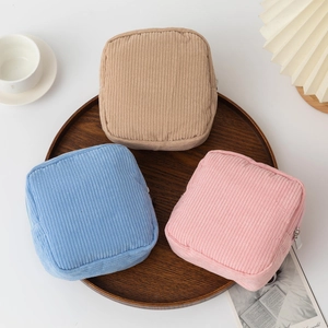 Minimalist corduroy makeup storage bags in soft blue, pink, and beige on a wooden tray
