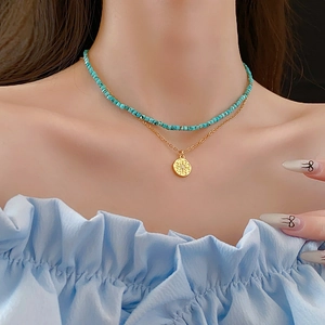Gros plan d'un collier double rang avec perles turquoise et pendentif soleil doré