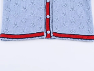 Detail of light blue knit cardigan with floral eyelet pattern and striped contrast trim