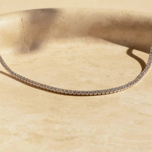Close-up of a silver tennis necklace with round rhinestones in a ceramic bowl