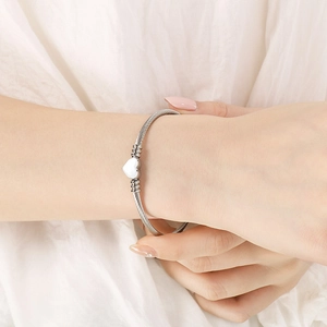 Bracelet câble en acier argenté avec breloque cœur porté au poignet sur tissu blanc