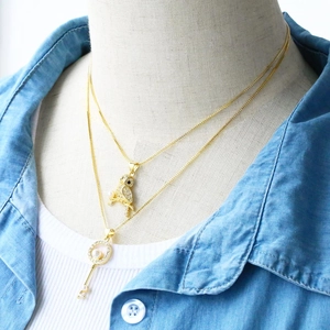 Detalle de collares dorados en capas con colgante de búho y llave de perla en modelo