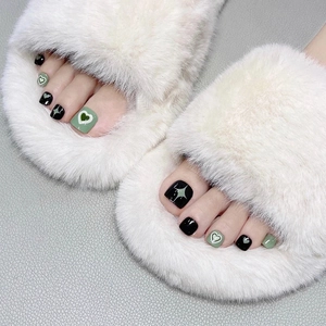 Detailed view of green and black heart-patterned press-on toenails on white plush slippers