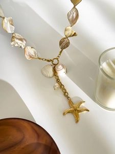 Detailed view of ocean-themed necklace with gold starfish and natural shell on a white stand