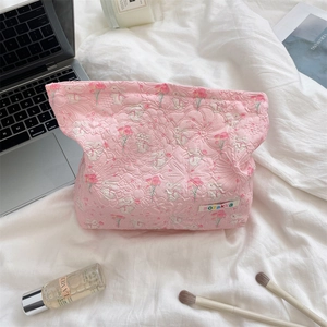 Pink quilted cosmetic bag with floral rabbit pattern on bed with makeup accessories