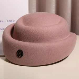Close-up of pink wool felt pillbox hat featuring a metallic black M logo on textured fabric