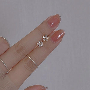 Macro shot of mini flower studs with zircons and twisted rope ring held by fingertips
