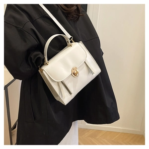 Close-up of white leather handbag with golden lock and adjustable strap detail