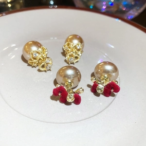 Macro shot of gold pearl crown and red bow earrings displayed on a white plate