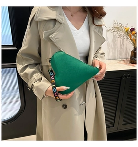 Detail of green heart-shaped pouch with textured leather and LOVE strap on beige coat