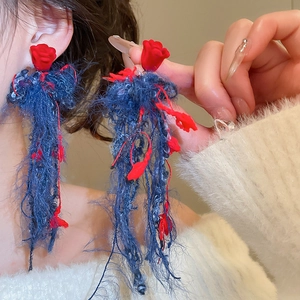 Dettaglio di orecchini a rosa rossa con lunghe nappe in filato blu e fiori decorati